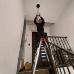 港区ビルのLED照明工事|脚立を使い階段の天井照明器具を取り付ける作業員