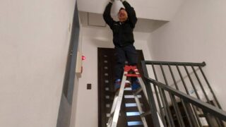 港区ビルのLED照明工事｜脚立を使い階段の天井照明器具を取り付ける作業員